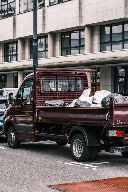 A white Toyota pickup truck with 'TOYOTA' branding and a removable tray loaded with household furniture, including a brown upholstered armchair and a wooden cabinet, is shown transporting items along