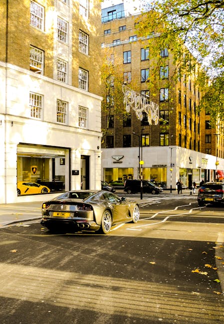 A street scene in Mayfair during daylight hours showing a variety of vehicles, including a black sports car with a sleek design and a visible license plate, parked near a sidewalk with a yellow sports